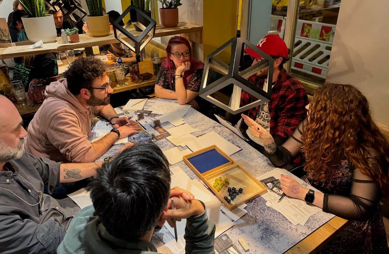 A table of happy, diverse gamers at BIRCON 2024, with another table visible in the background.